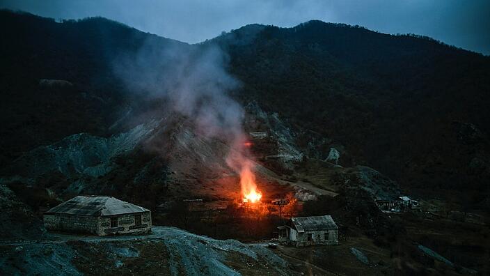 It is night. In the mountains in the region of Nagorno-Karabakh, there are isolated stone houses. A large fire lights up the surrounding area.