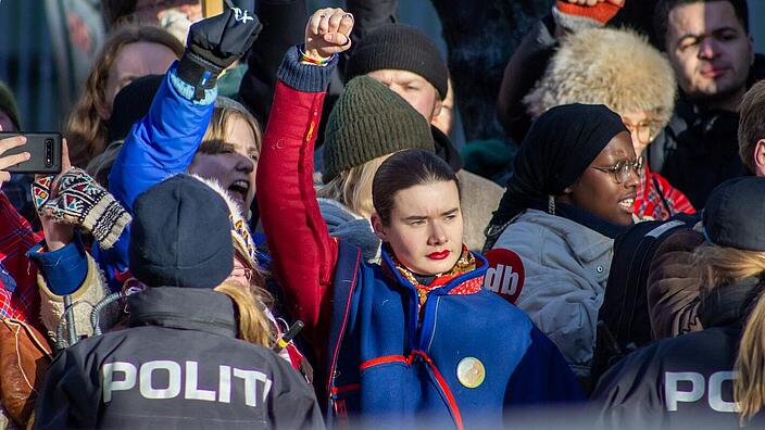 Young woman with raised fist in a crowd of people, police officers next to her